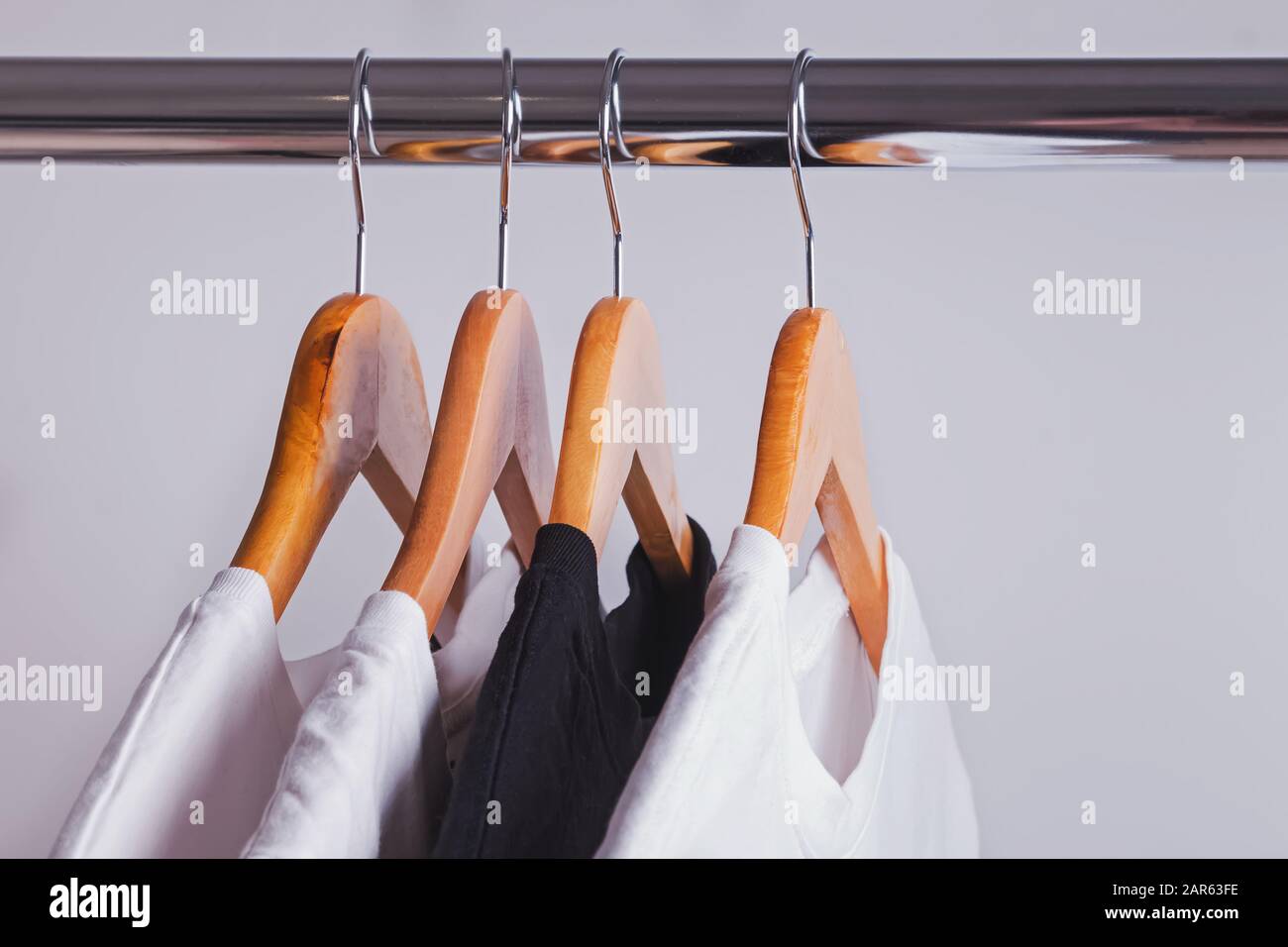 One black t-shirt in a row of white shirts hanging on wooden hangers Stock Photo