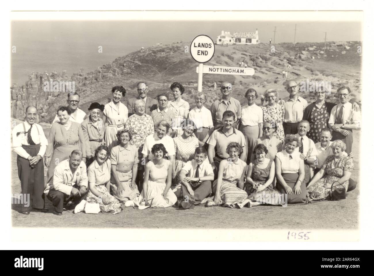 1950's commercial photo of day trippers group on holiday from Nottingham pose for a photo next to the famous signpost at Land's End, Cornwall, U.K. dated August 1955 Stock Photo
