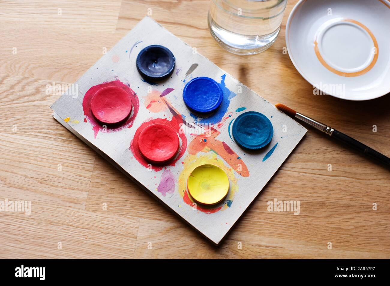 Watercolor paints with brush, plate and glass jar on the wooden table. Stock Photo