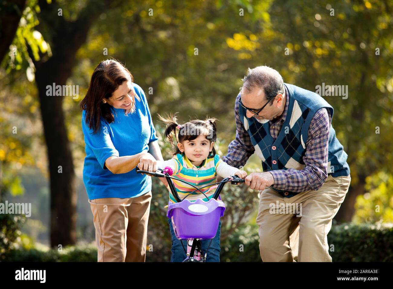 Grandparents with granddaughter learning to ride bicycle Stock Photo