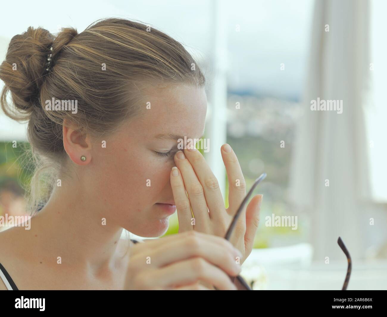 A woman has taken off her glasses and presses her fingers on the closed corners of her eyes because she is tired, unfocused and exhausted. Stock Photo