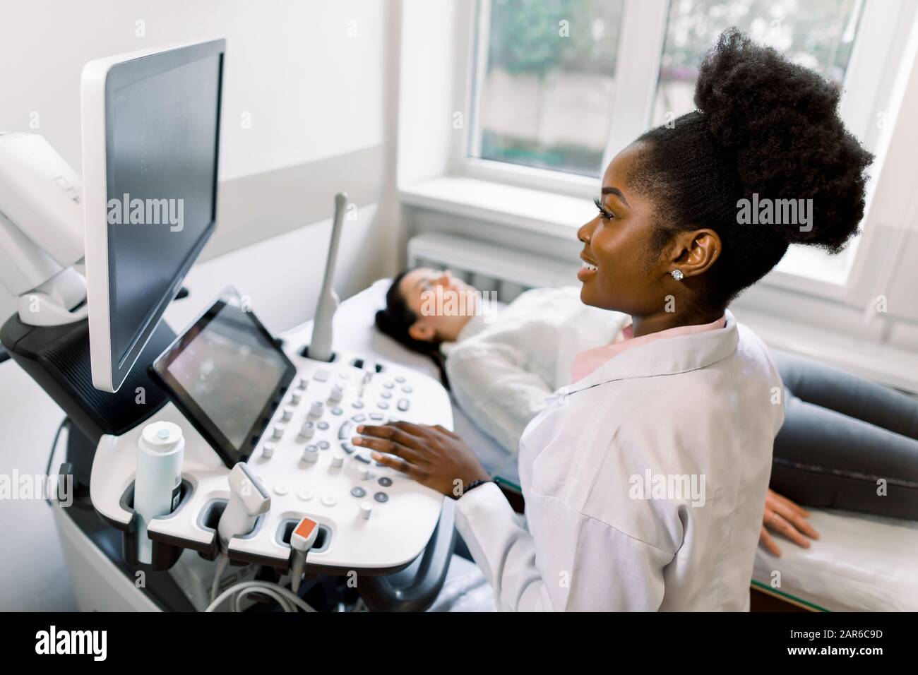 Young African female doctor using ultrasound machine in clinic, makes