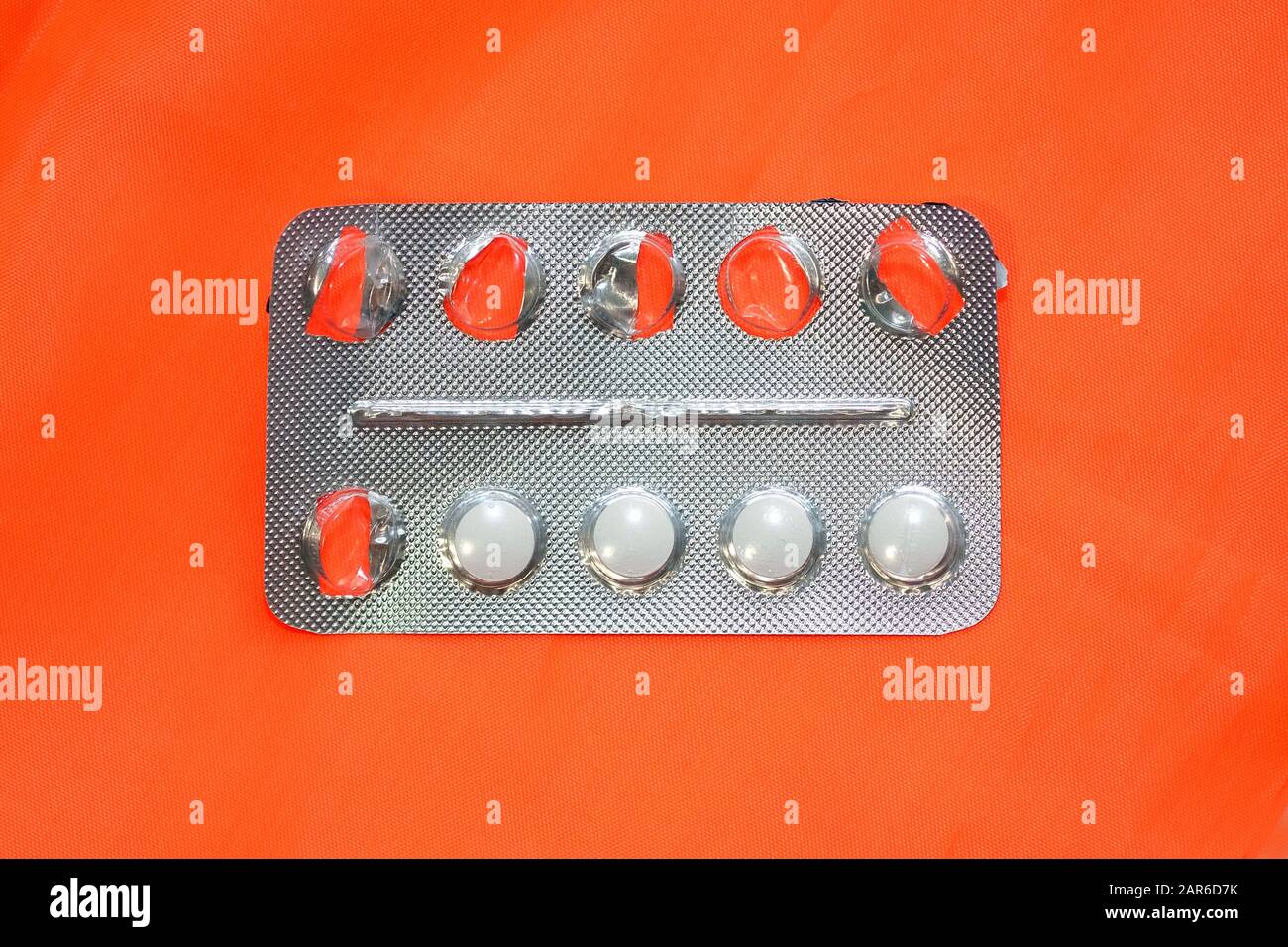Gray blister with white pills on an orange background. Half empty pack with pills. Round white allergy pills. Stock Photo