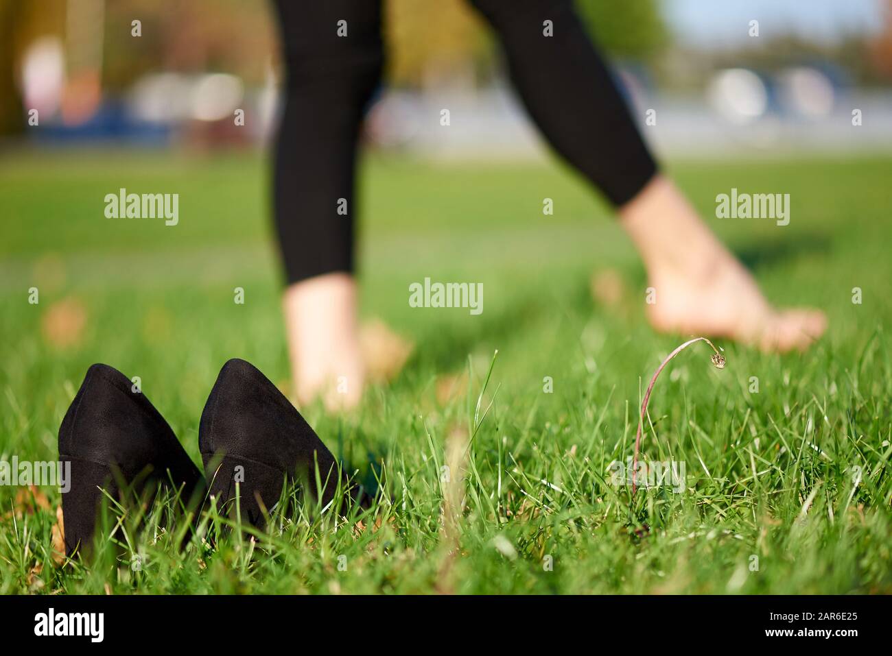 Black shoes in the grass on a background of barefoot female legs Stock