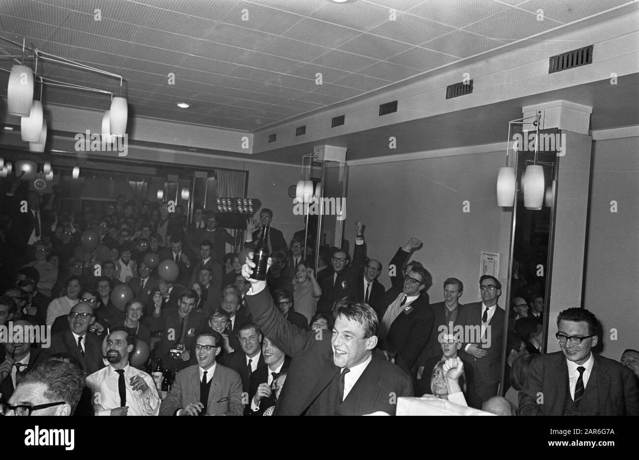 Hans van Mierlo, voorzitter en lijstaanvoerder van D66, blij met de verkiezingsuitslag. Van Mierlo heft juichend zijn arm met een flesje bier, in de overvolle Kleine Zaal van Hotel Krasnapolsky te Amsterdam, Nederland 15 februari 1967.; ' Stock Photo