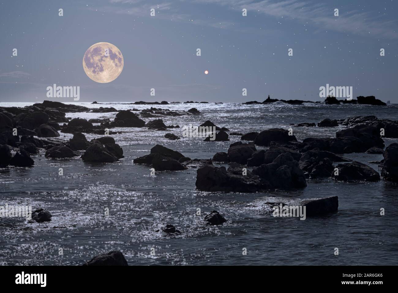 Moonlit rocky coast in a full moon starry night just before dawn in ...