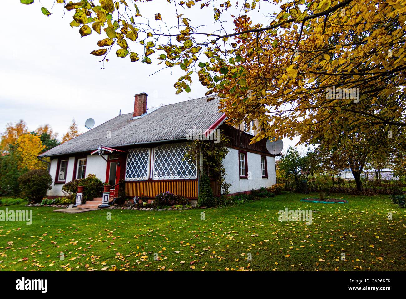 A Lithuanian cottage outside of Silute. Beautiful green grass and yellow leaves cover the floor. Stock Photo