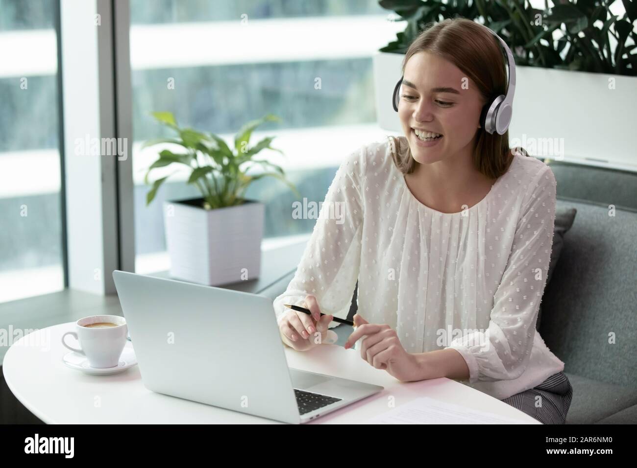 Happy young employee wearing wireless headphones, holding video call ...