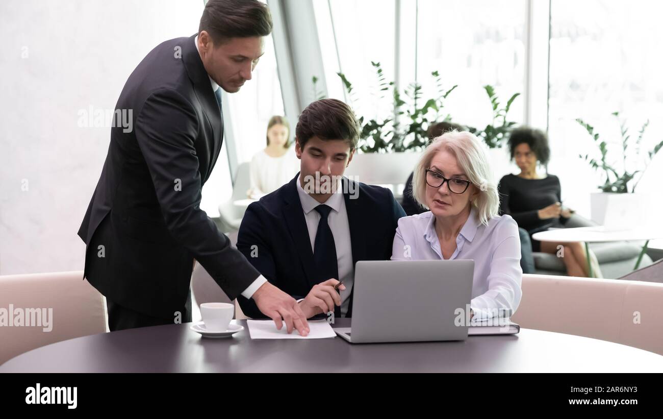 Confident male supervisor helping different ages teammates. Stock Photo