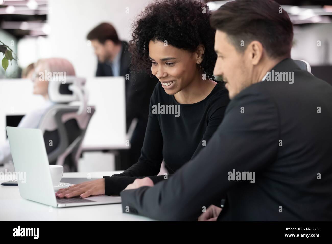 Happy multiracial colleagues managing project on laptop at workplace ...