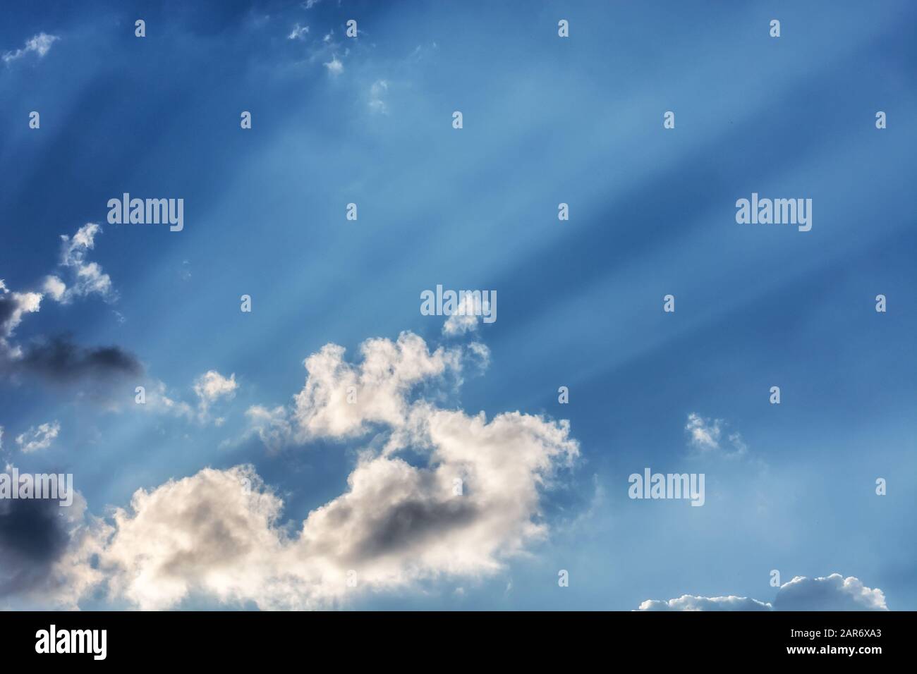 Rays of the sun breaking through the clouds against a bright blue sky, for use as an abstract background and texture. Stock Photo