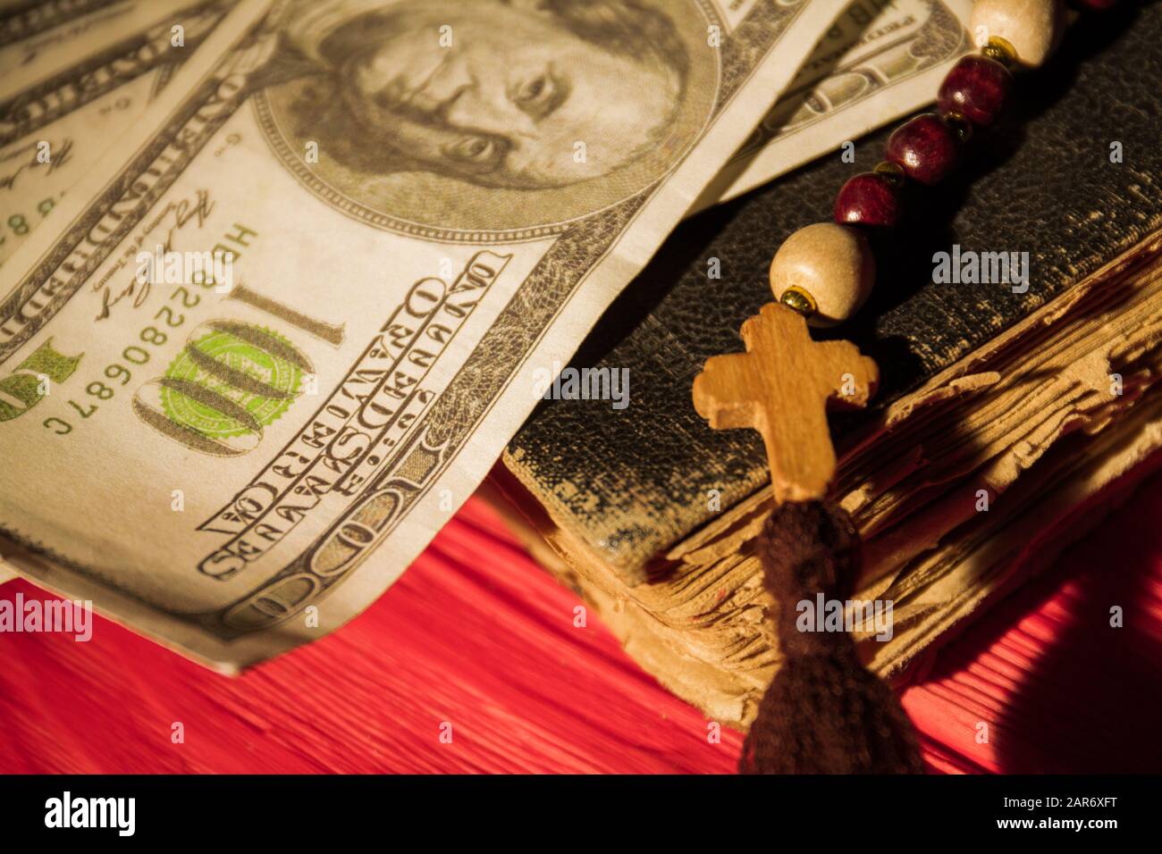 Close up old book, wooden cross on bead necklace and money. Stock Photo