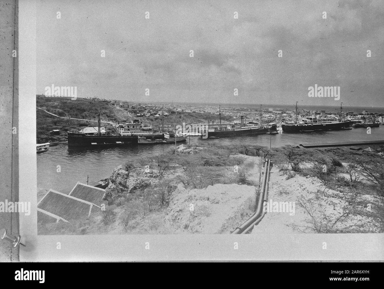 Wi [West Indies]/Anefo London series  [Dutch West Indies. Curacao. View of Willemstad's St Annahaven, which connects the Schottegat lagoon to the ocean. The cargo ship in the middle is moored at one of the docks of the Curacao Handel Maatschappij. The pipelines lead to Caracas bay] Annotation: Repronegative Date: {1940-1945} Location: Curaçao, Willemstad Keywords: ports, ships, World War II Stock Photo