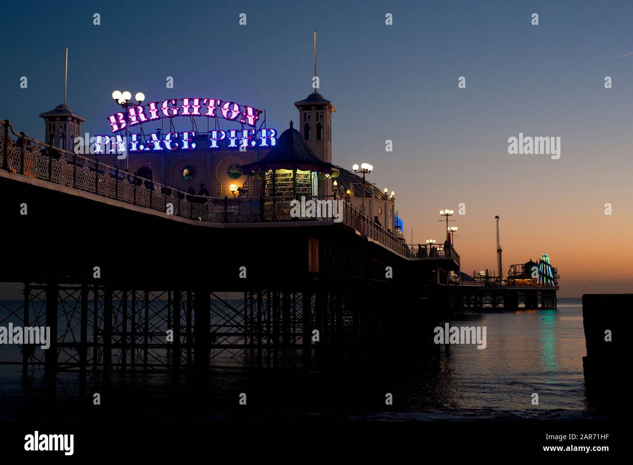 Brighton Palace Pier with its illuminated sign lit up at dusk. The famous pier is one of the U.K.'s most visited tourist sights. Stock Photo