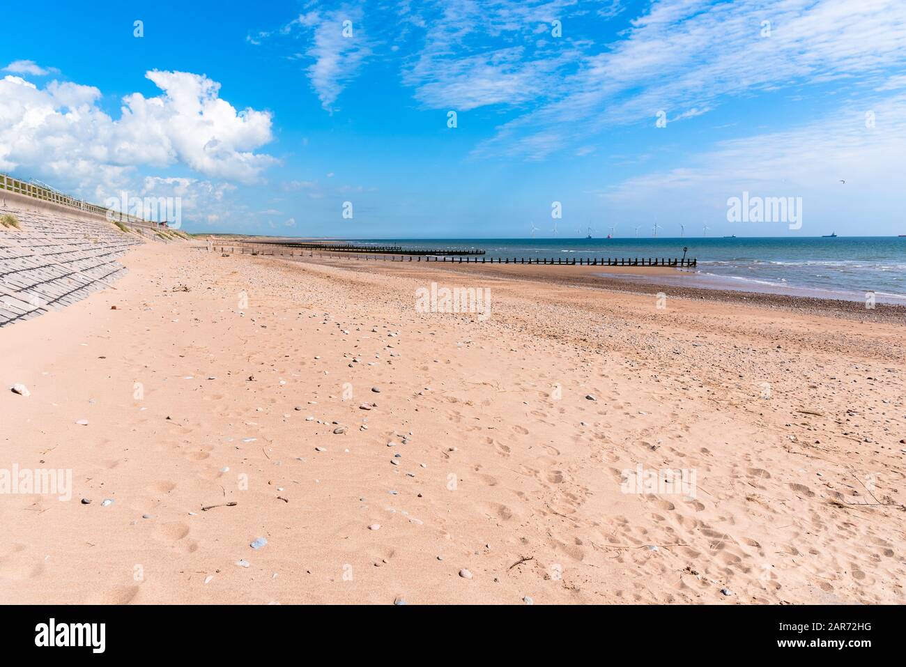 Deserted sandy beach facing an offshore wind turbines on a sunny spring day Stock Photo