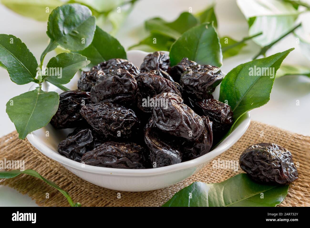 bowl of sweet dried plums with lemon leaves on a white background Stock Photo