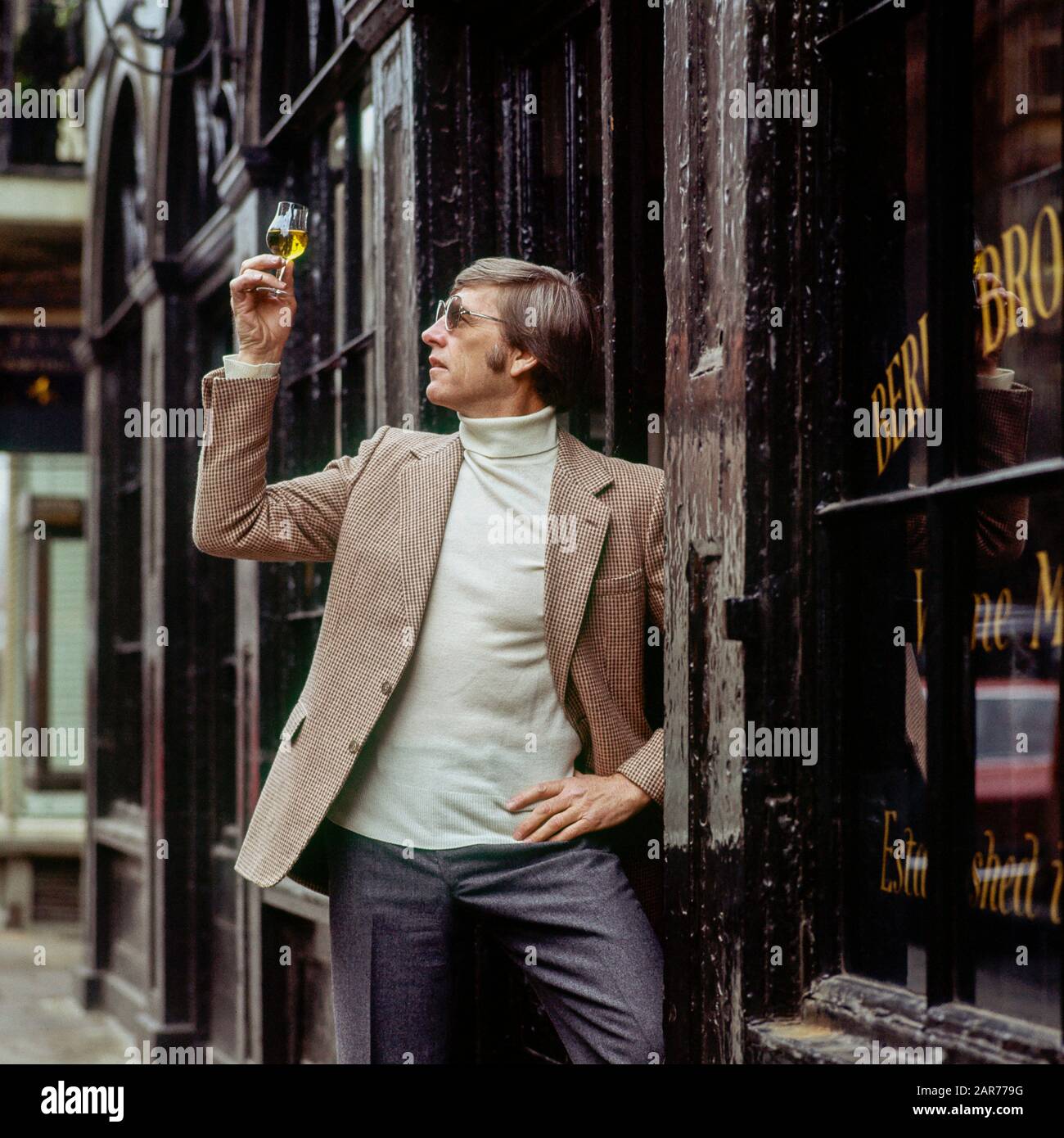 London 1970s, man examines a sherry wine glass outside Berry Bros. & Rudd wine merchants store, St James street, England, UK, GB, Great Britain, Stock Photo