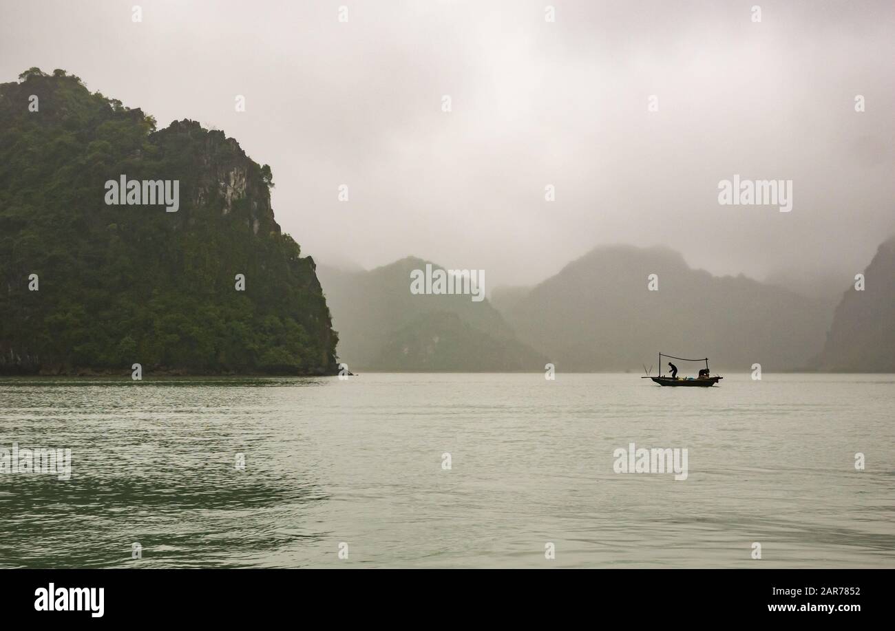 Small fishing boat in Halong Bay in foggy weather with limestone karst mountains, Vietnam, Asia Stock Photo