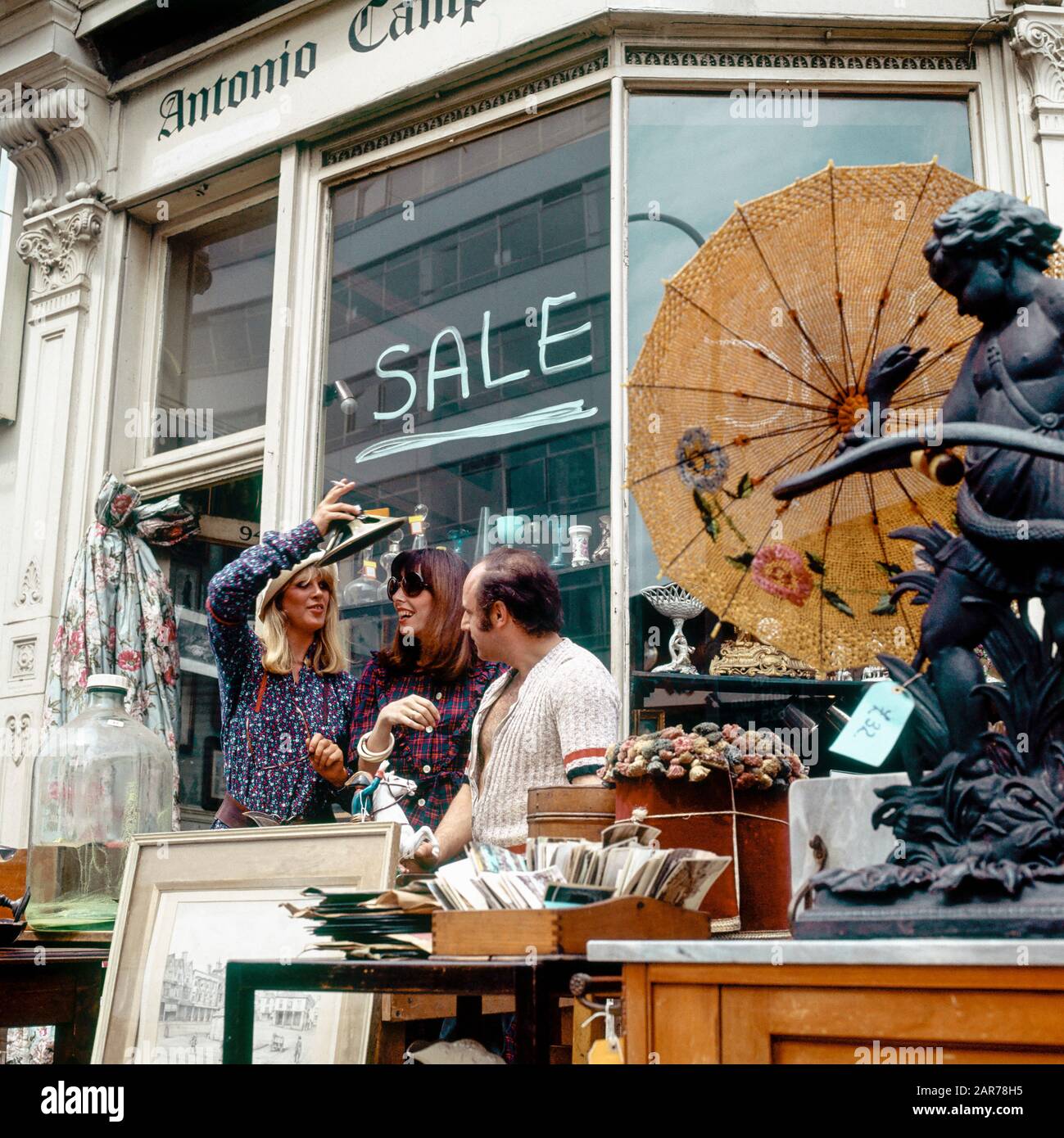 London 1970s, two women having fun with merchant while shopping at antiques store, Kensington, England, UK, GB, Great Britain, Stock Photo