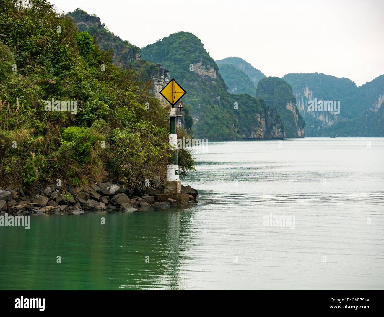 Navigational marker on rocky shore with limestone karst cliffs, Halong Bay, Vietnam, Asia Stock Photo