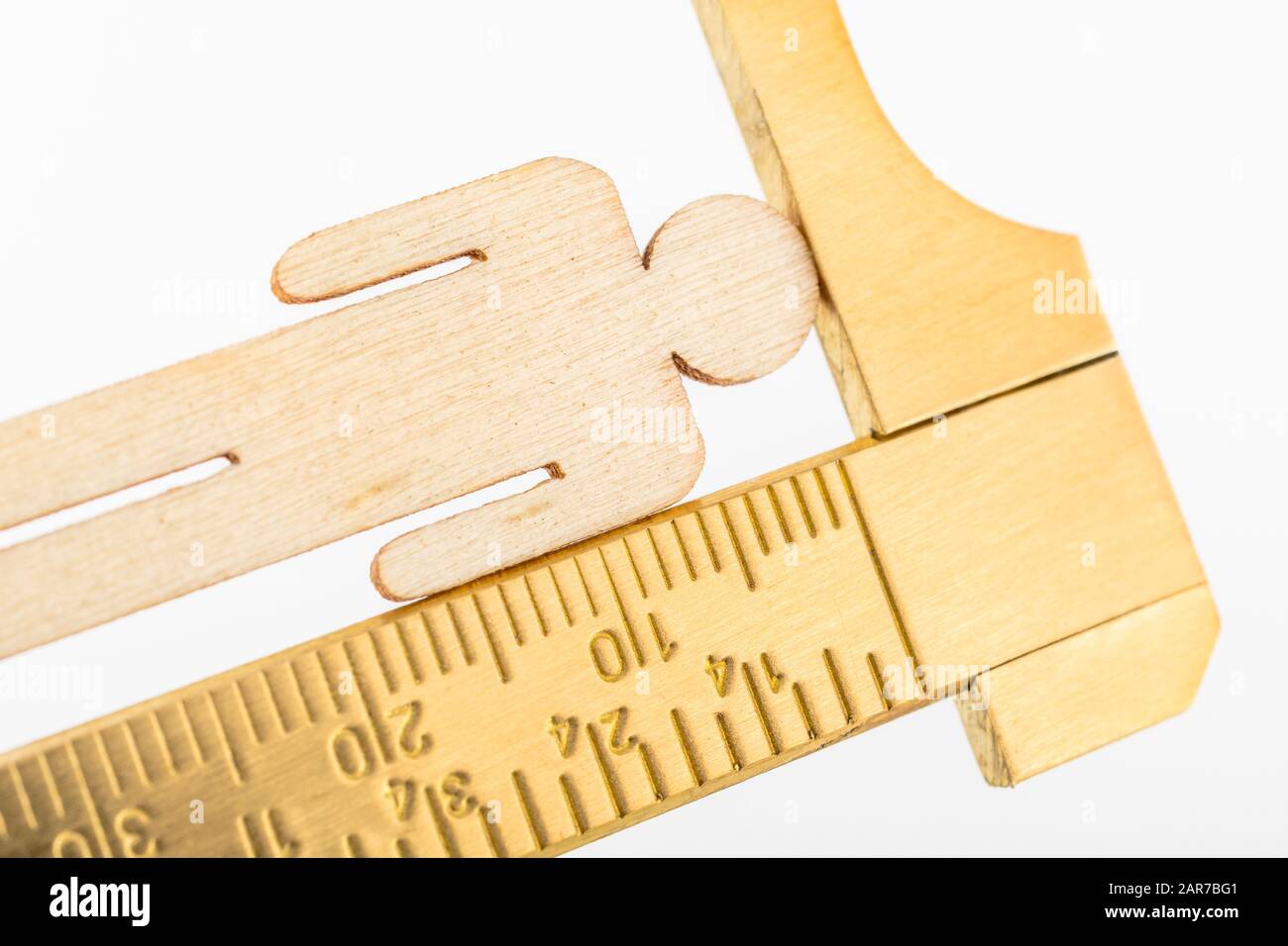 Macro small laser-cut wooden figure & brass calipers against off-white ...
