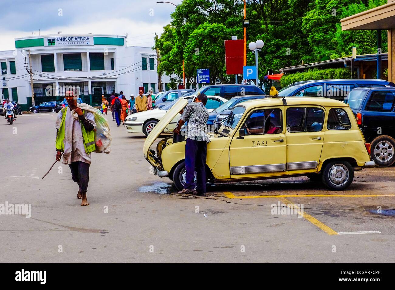 A man walks past a taxi-driver repairing his taxi in Antananarivo, the capital of Madagascar. Stock Photo