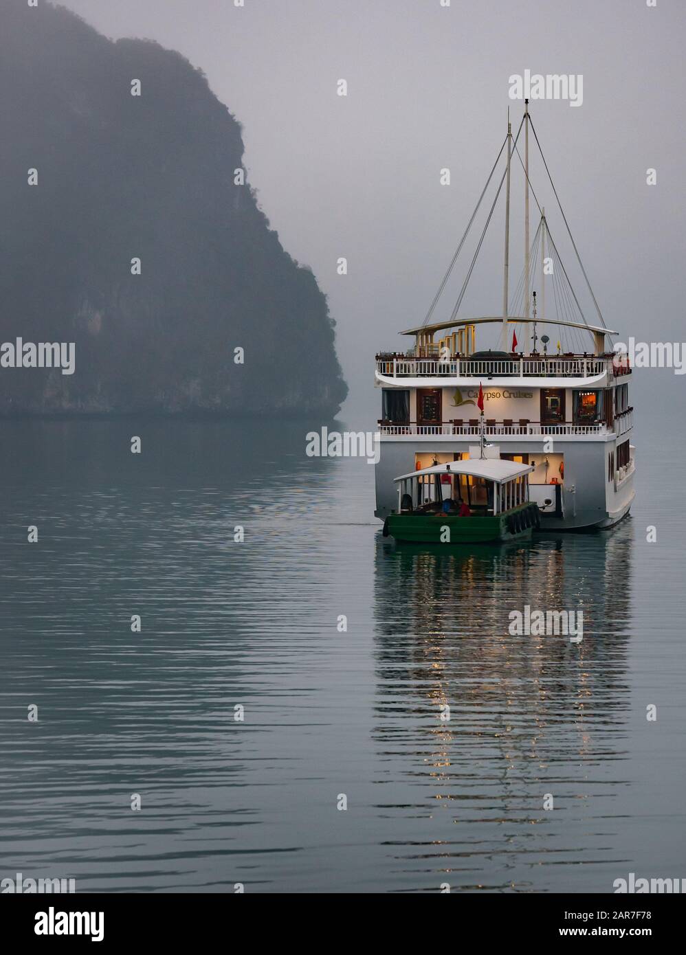 Tourist Calypso cruise ship & tender anchored at dusk in misty weather, Halong Bay, Vietnam