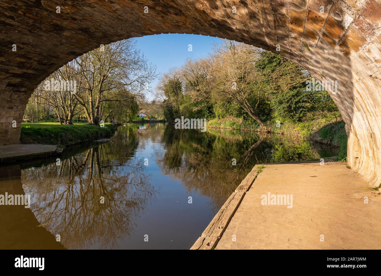 The River Nene at Wansford, Cambridgeshire, England, UK, with Jurassic limestone bridge on a calm, sunny day in April and reflections in the water Stock Photo
