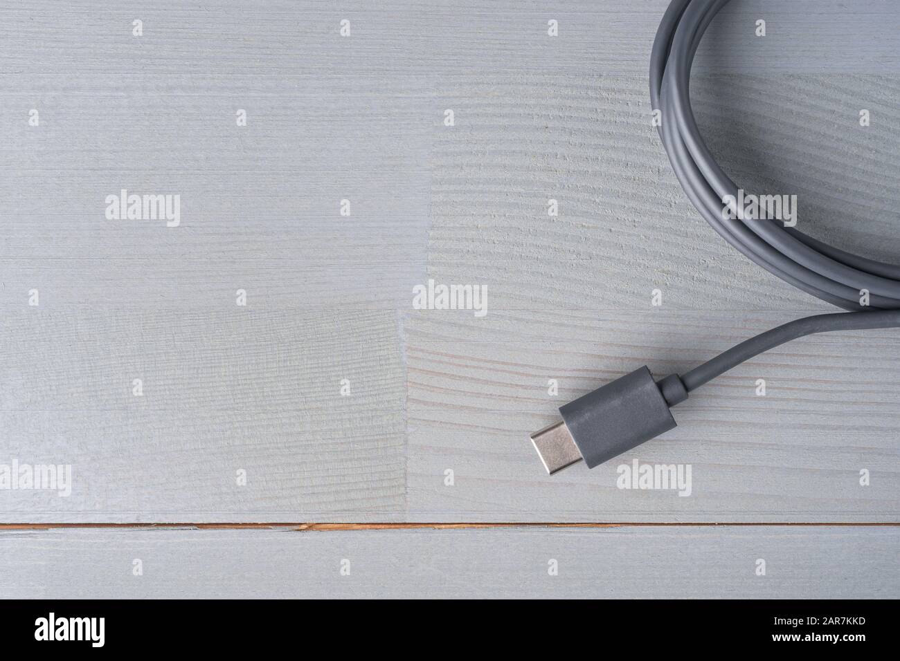 USB Type C connector with a grey cable on a wooden background. Flat lay top view. Large copy space on the left. Stock Photo