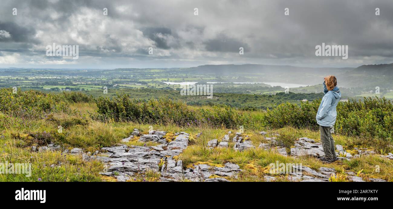 A female tourist takes in the view from Parknabinna in the limestone pavement of the Burren over the sandstone and shale country of south Clare Stock Photo