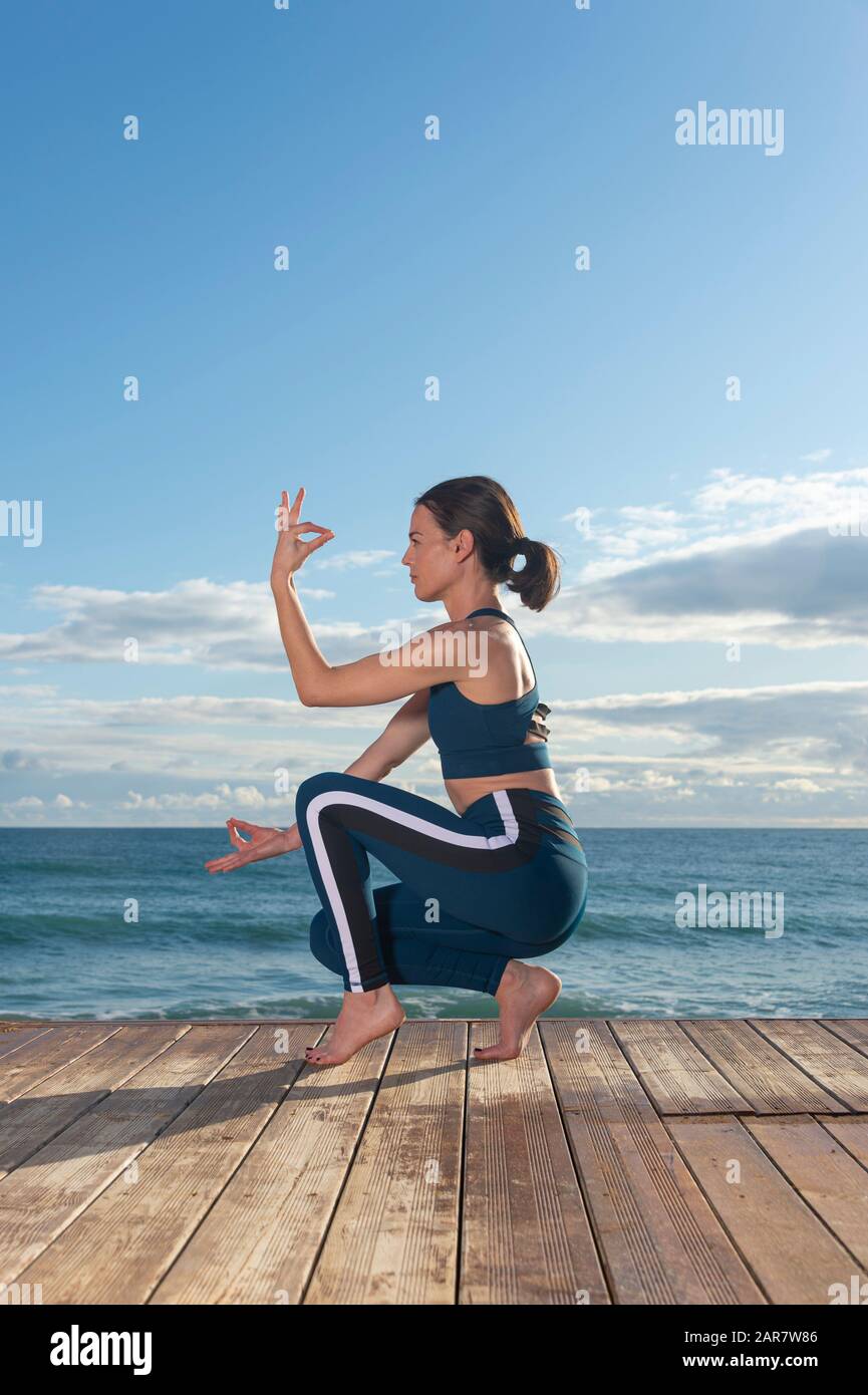 fit woman practicing yoga outside by the ocean, toe balance. healthy lifestyle. Stock Photo