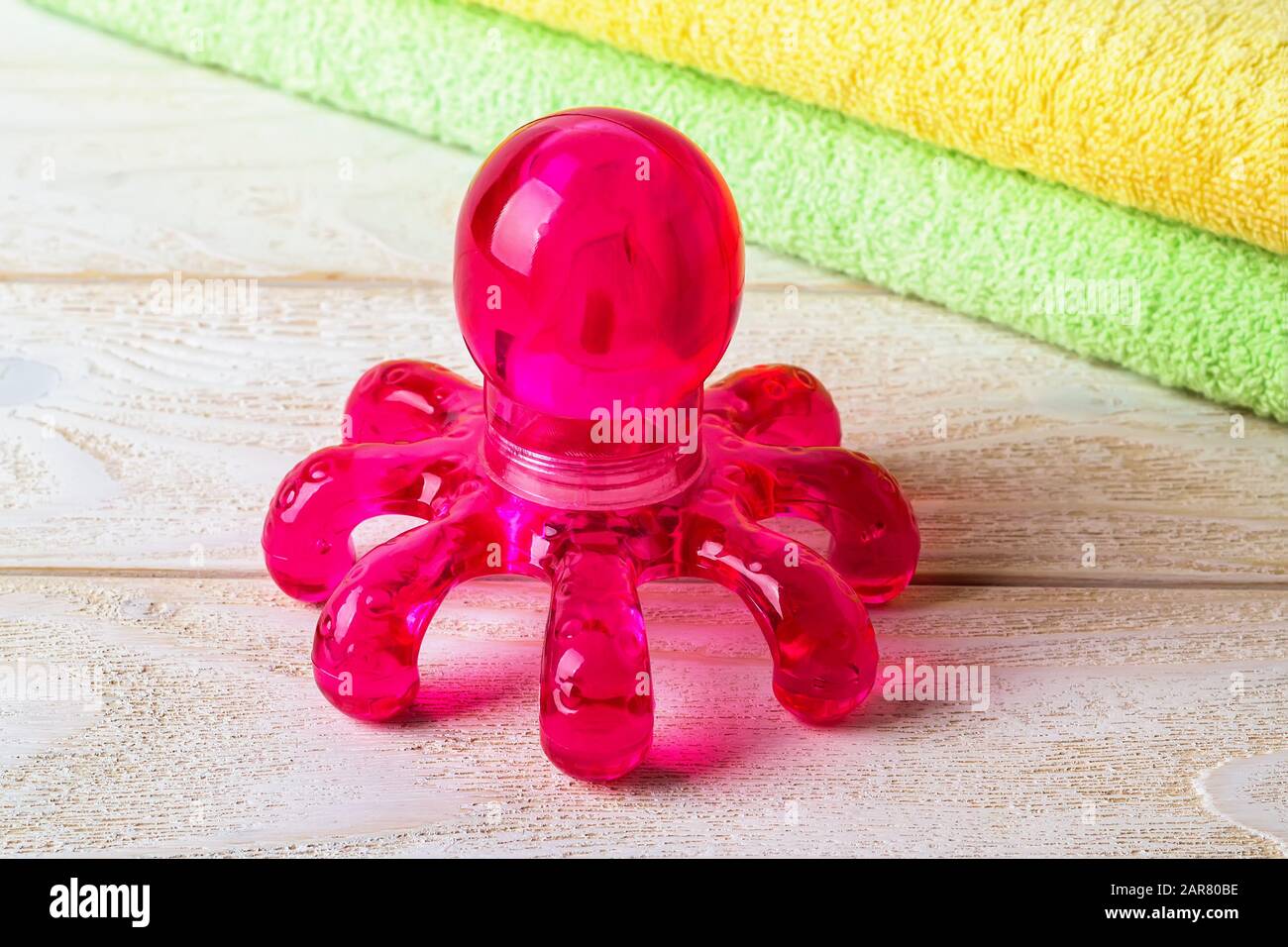 Red plastic spa massager in the form of an octopus on a white wooden surface. Massage handheld tool for limbs and body. Front. view. Stock Photo