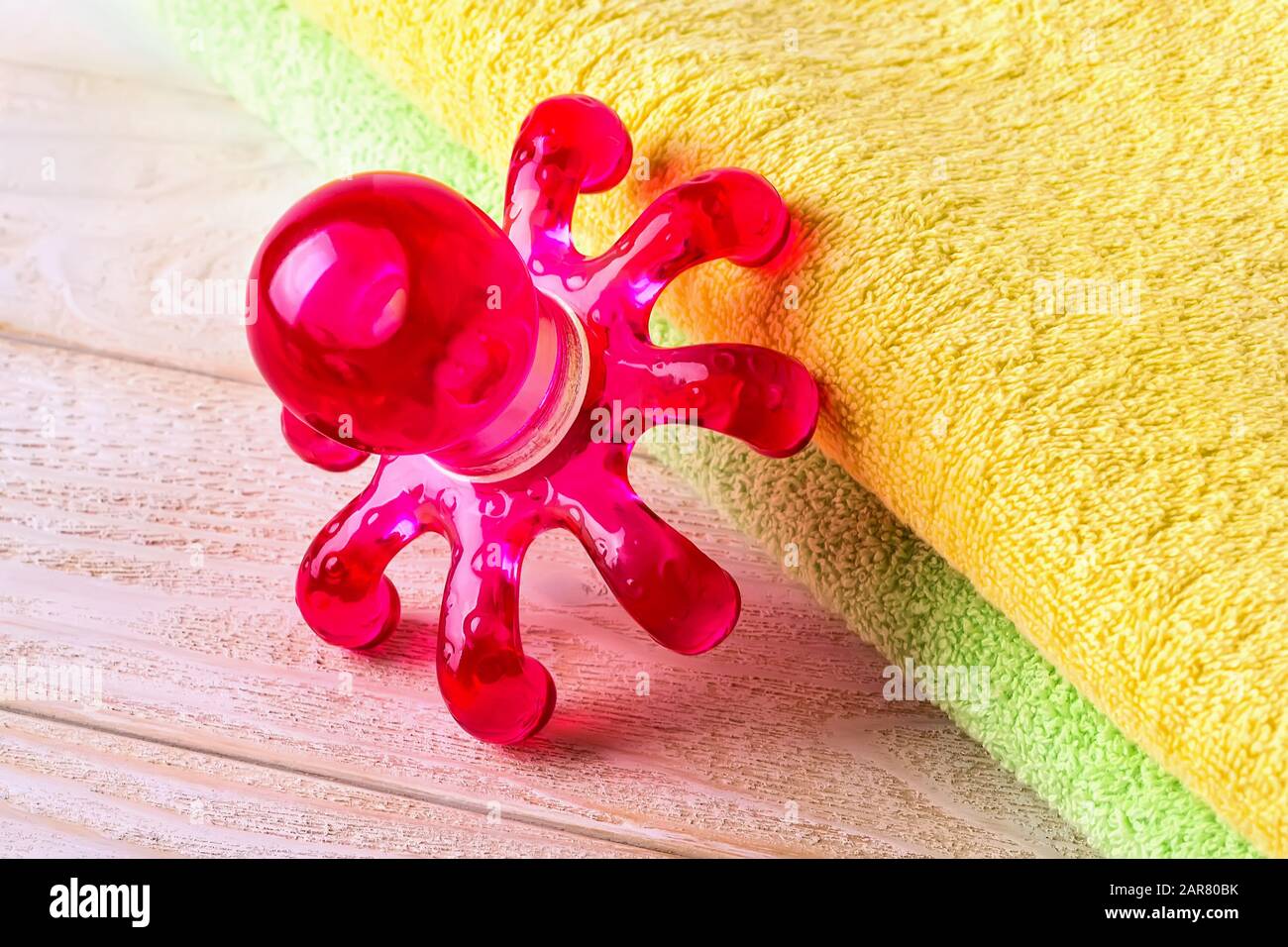 Massage handheld tool on a white wooden surface. Red plastic spa massager in the form of an octopus for limbs and body. Front. view. Stock Photo