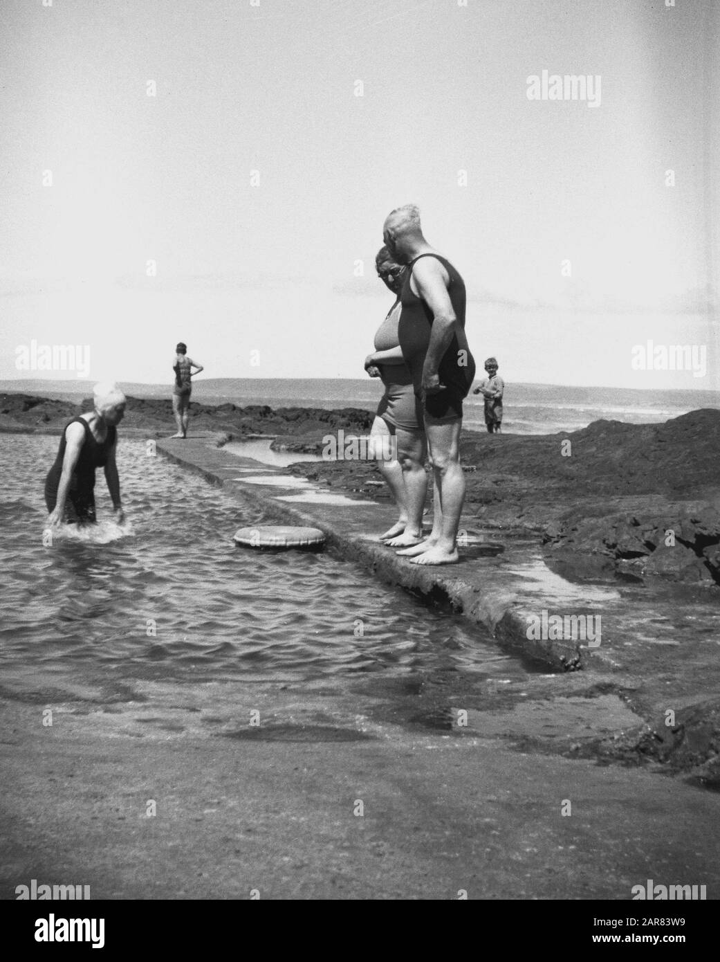 1930s, historical, male and female adult bathers in the swimming costumes of the era in a sea pool at the coast, Bideford, Devon, England, UK. Partially man-made open-air tidal swimming or paddling pools of sea water built by rocks were a feature seen at coastal areas in Devon and Cornwall. Stock Photo