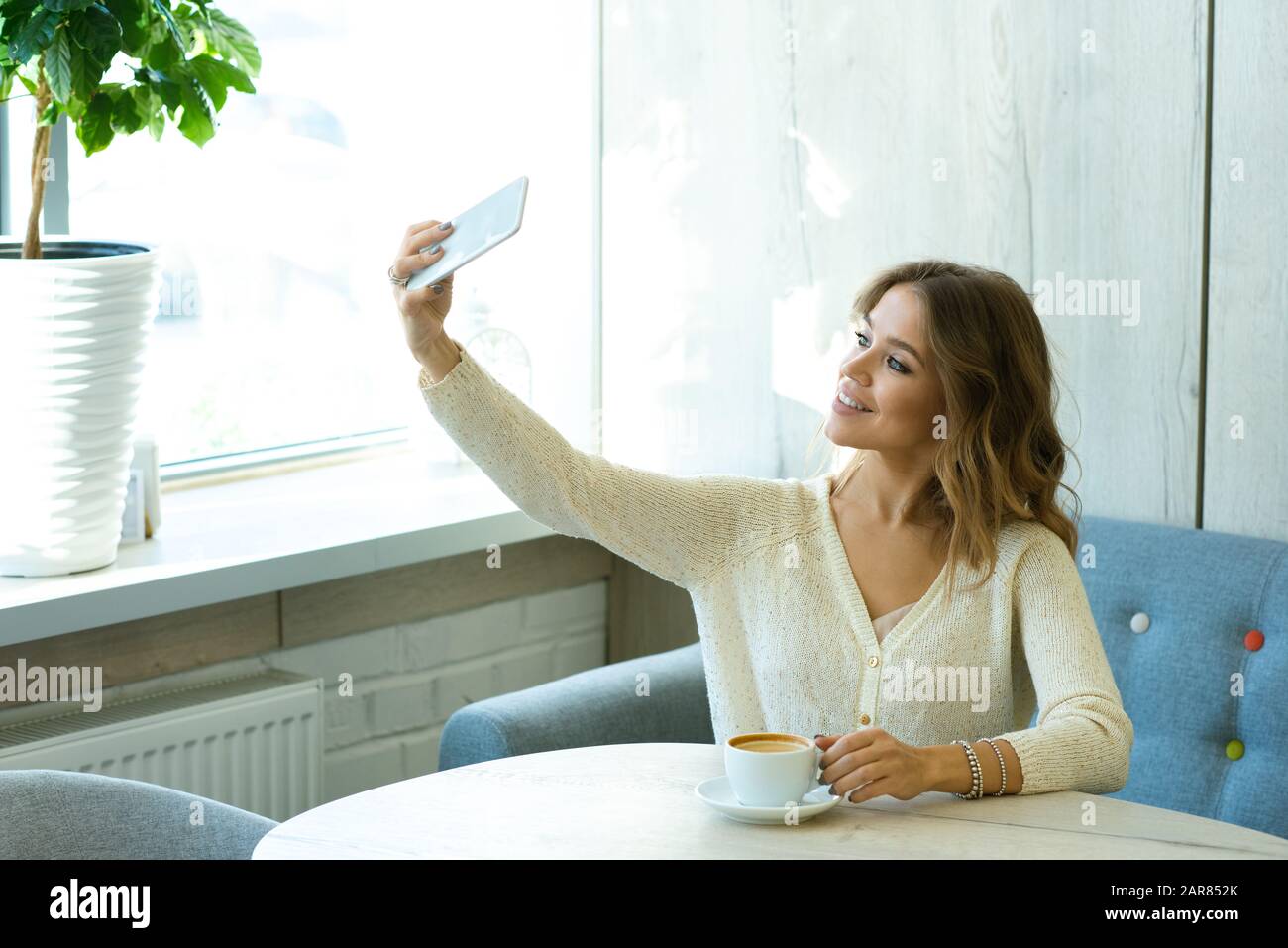 Pretty young smiling woman with smartphone making selfie while resting in cafe Stock Photo
