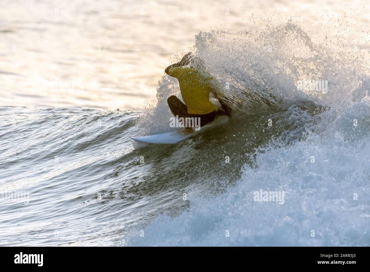 Surfer contestant in yellow jersey has head covered in white water spray while riding an ocean wave. Stock Photo