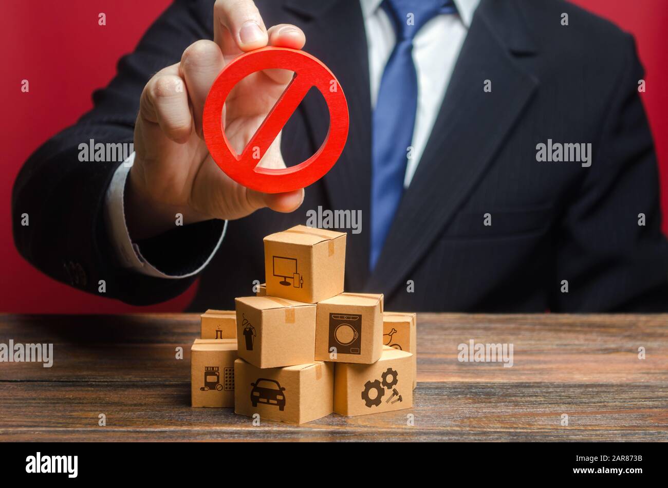 Businessman man official holding red prohibition sign NO over boxes with goods. Restriction import, ban export of dual use goods to countries under sa Stock Photo