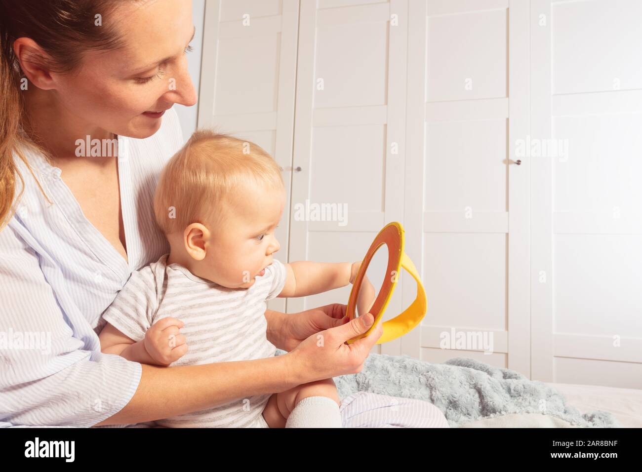 Mother and infant baby look at mirror together sitting in home