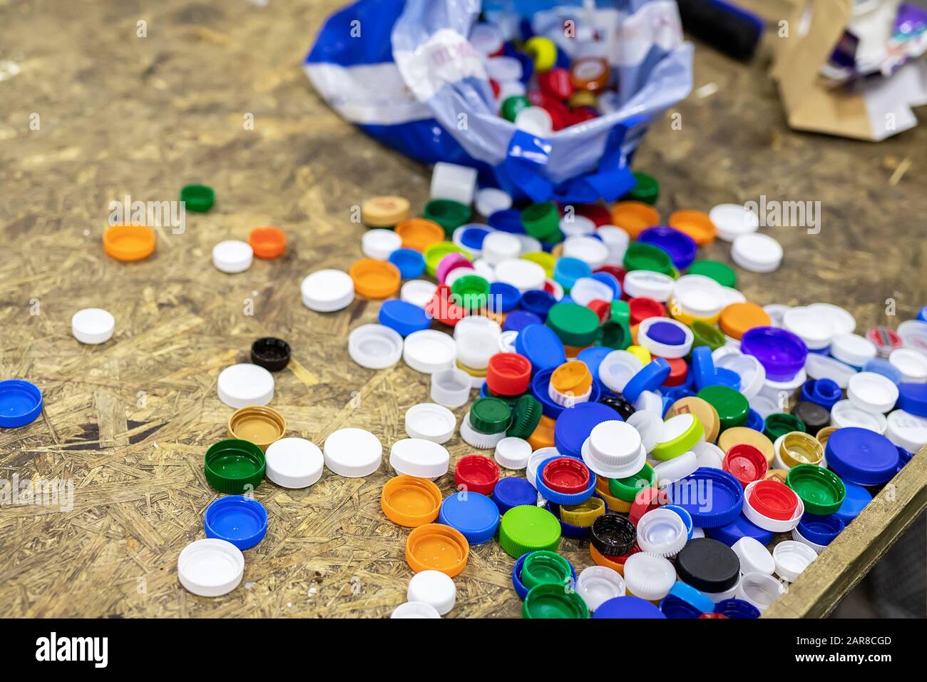 Pile of multicolored plastic bottles cap on chipboard wooden table at recycling disposal garbage