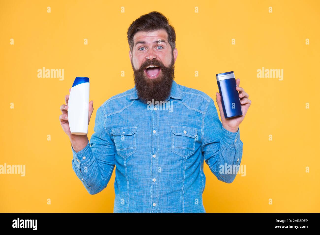 Grooming at every opportunity. Bearded man hold shampoo bottles yellow background. Cosmetics and