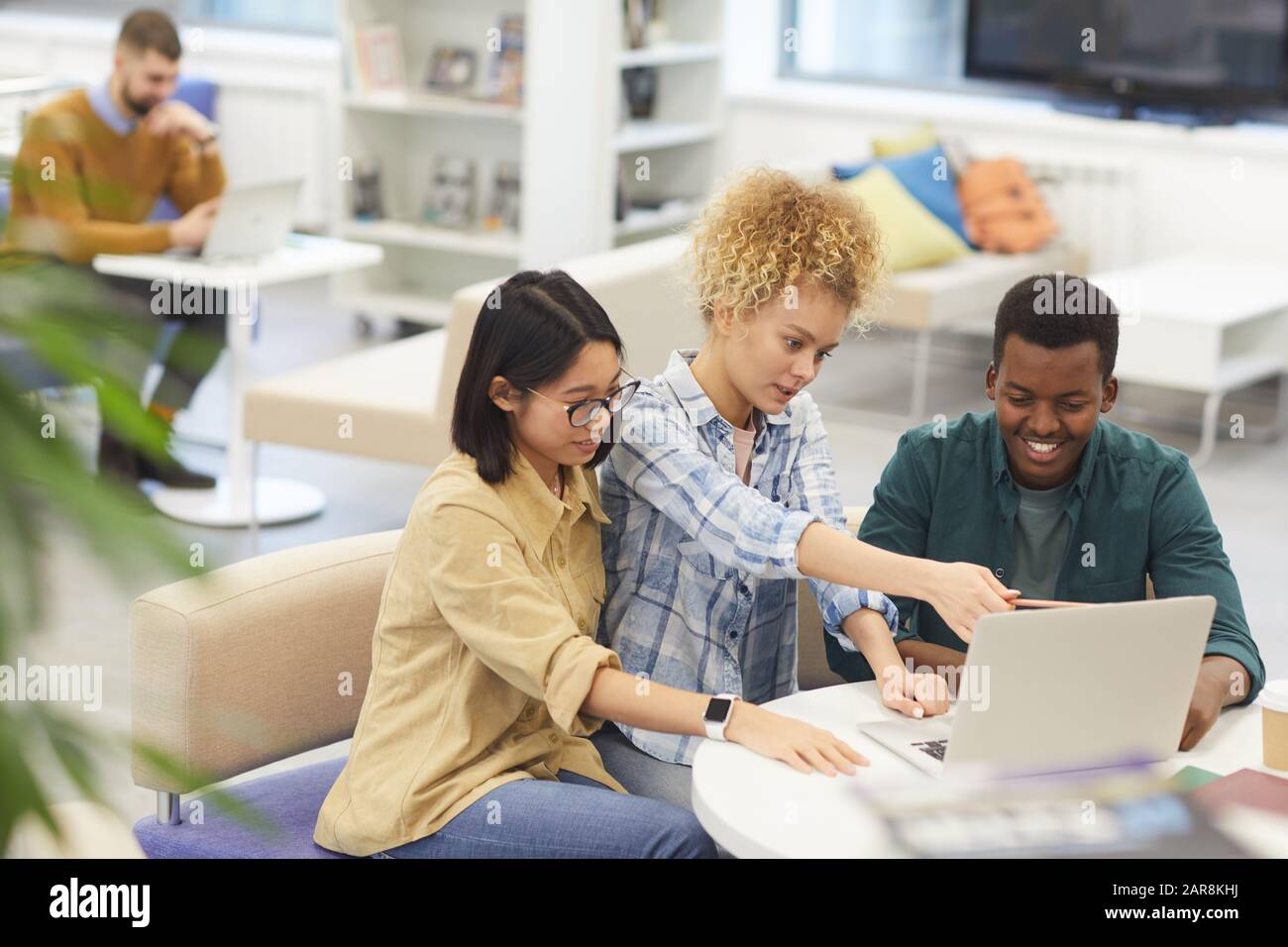 High angle view at multi-ethnic group of cheerful students using laptop together while working on project in library, copy space Stock Photo