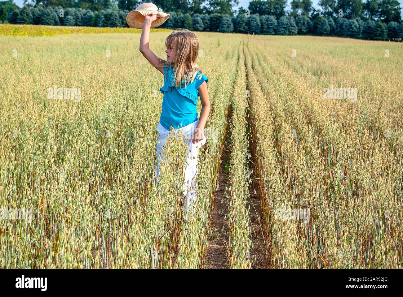 young blond Caucasian girl wearing white skirt and holding a hat walking in winter wheat field Stock Photo