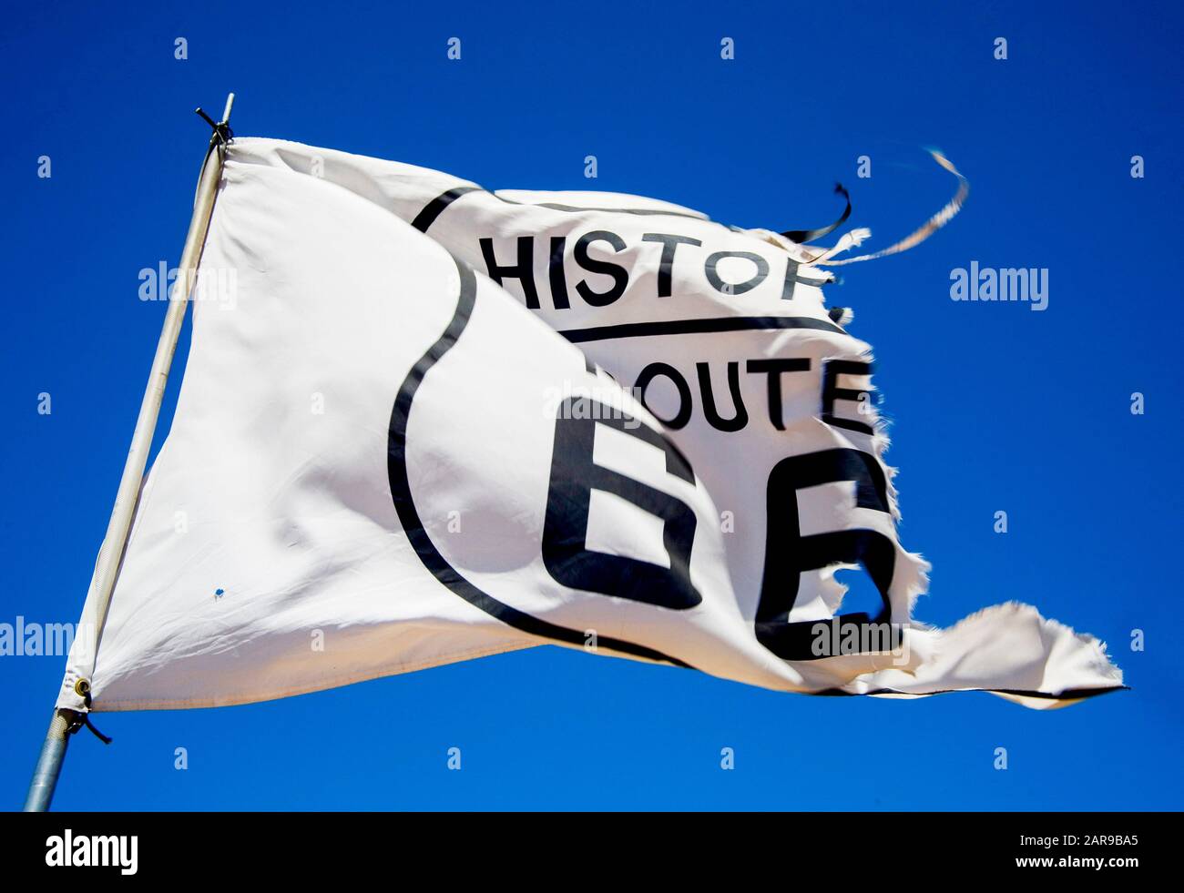 A tattered roadside flag blows in the desert wind outside of Flagstaff, AZ, proudly proclaiming the road to be part of Historic U.S. Route 66. Route 66, the so-called 'Mother Road,' is probably the most famous highway in the US. It has been superseded by the Interstate Highway Network. Stock Photo
