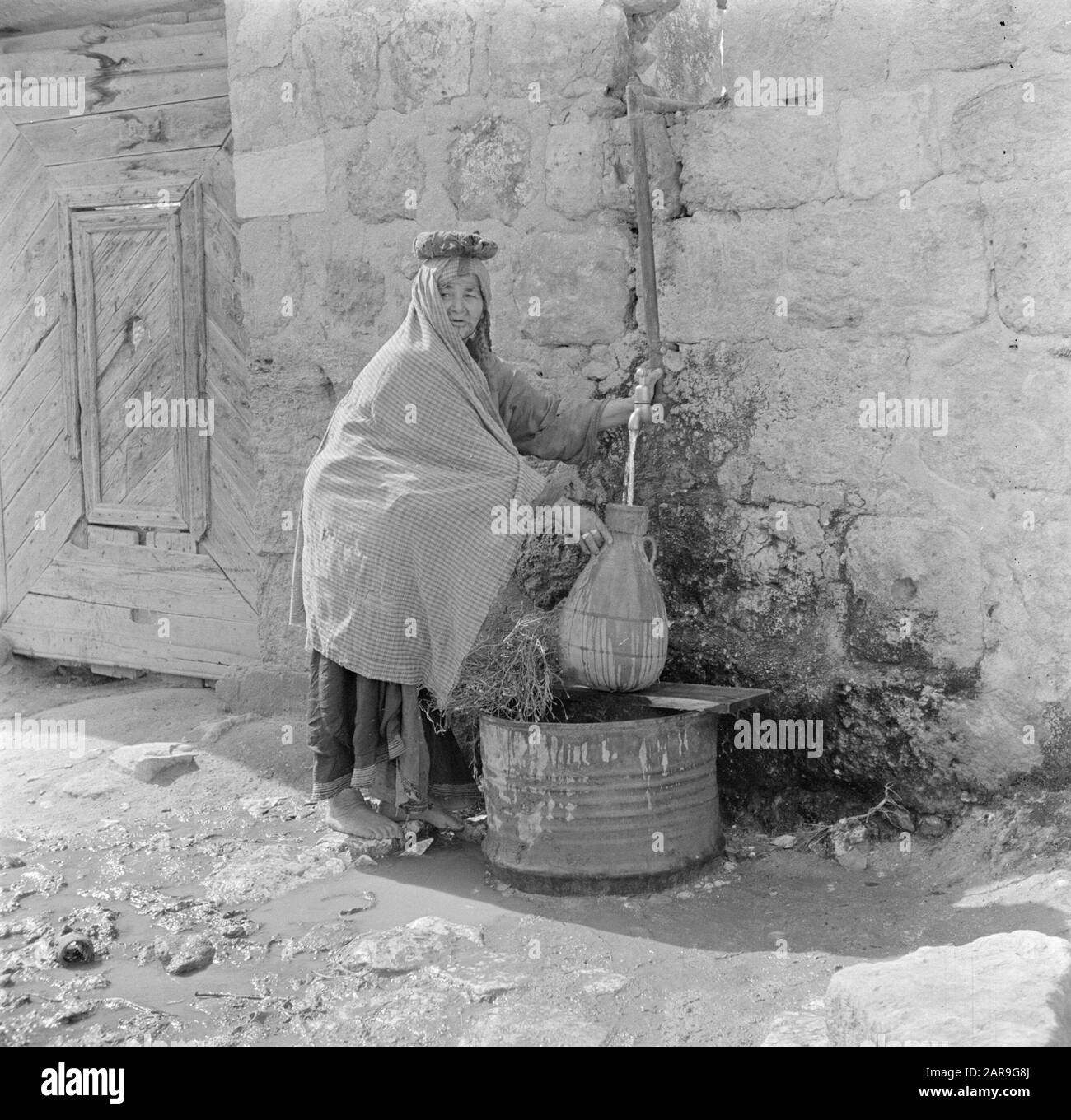 Israel 1948-1949: Lydda (Lod)  Woman taps water at a tap Date: 1948 Location: Israel, Lydda Keywords: village images, drinking water, utensils, women Stock Photo
