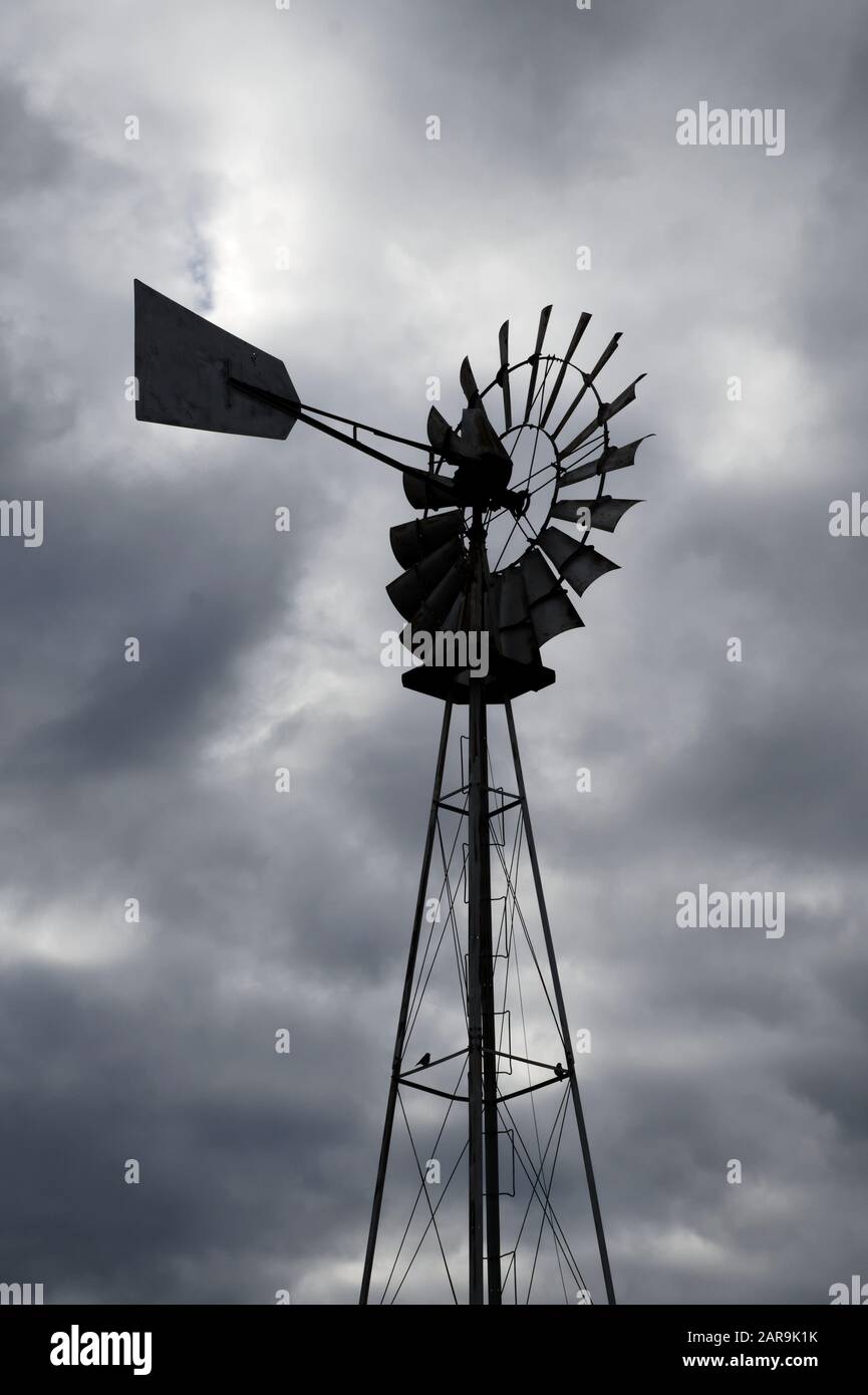 Old fashioned galvanized metal farm windmill for pumping water, as seen on a cloudy day Stock