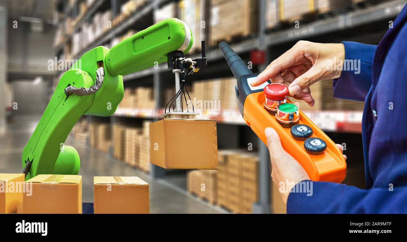 Industrial robot holding a box and worker operating a robot machine with a control panel on stock shelves background Stock Photo
