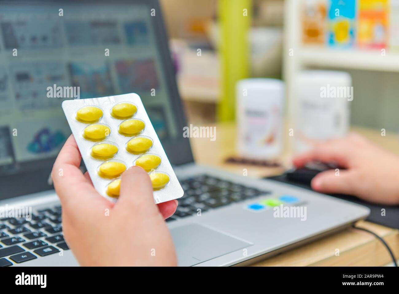 Pharmacist using the computer laptop in chemist shop or pharmacy drug store. Hand holding medicine pack and key the prescription order. Stock Photo