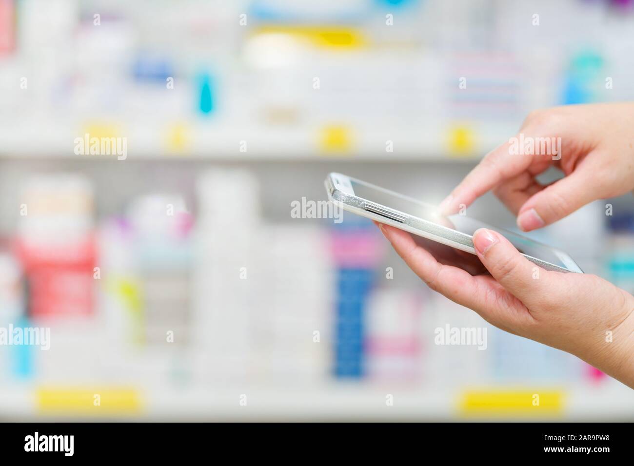 Pharmacist using mobile smart phone for search bar on display in pharmacy drugstore shelves background.Online medical concept. Stock Photo