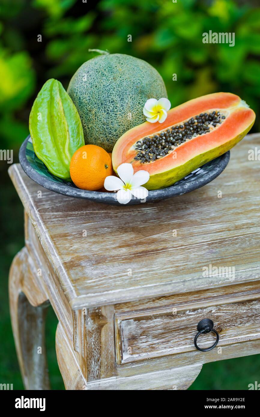 Fruit plate with fresh Bali fruits papaya, orange, melon and star fruit on  wooden vintage table in tropical garden. Frangipani flowers Stock Photo -  Alamy
