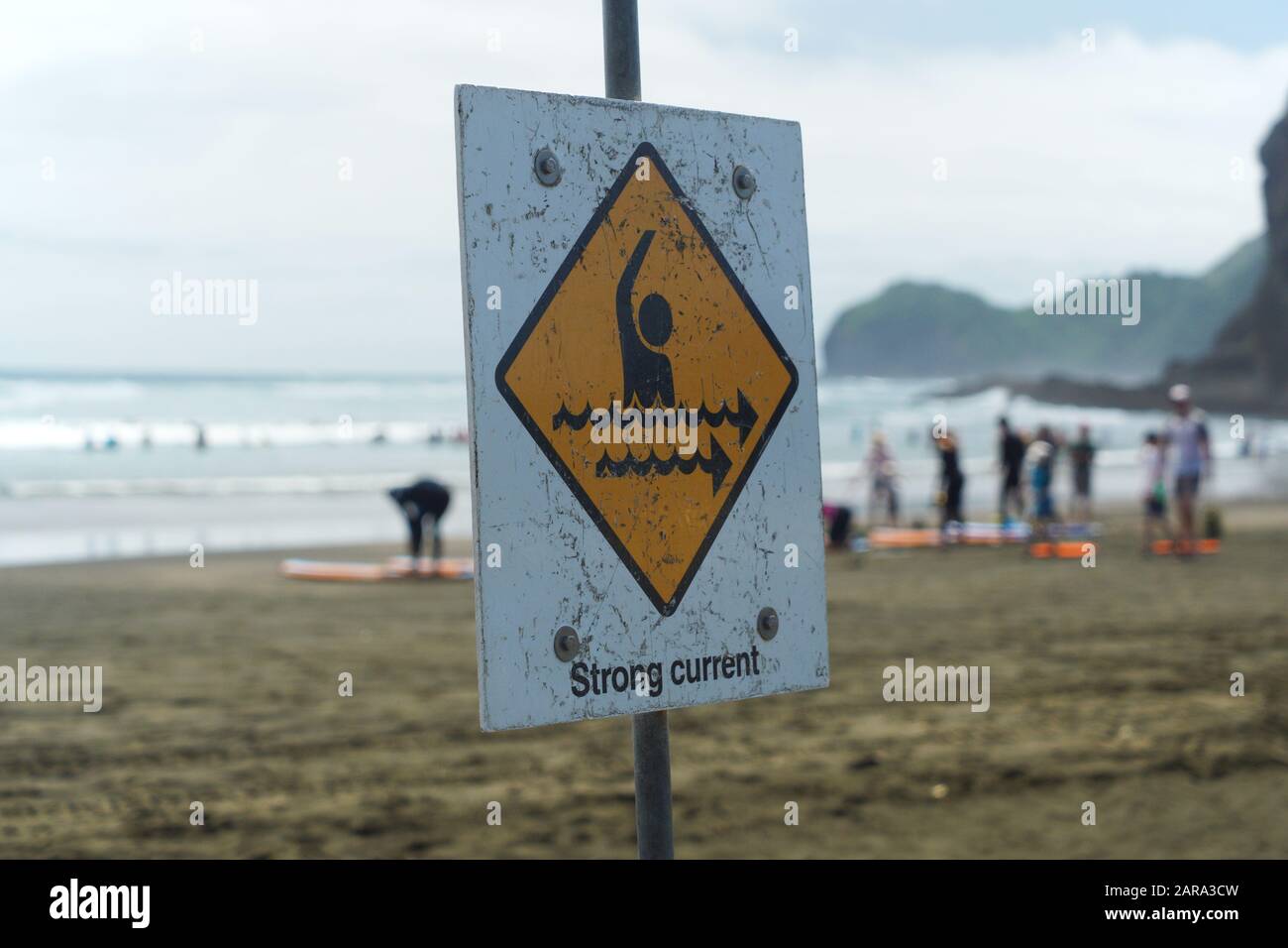 Piha South Beach, Auckland West Coast New Zealand. Summer day. strong current white and yellow lifeguard warning sign People taking surfing lesson Stock Photo